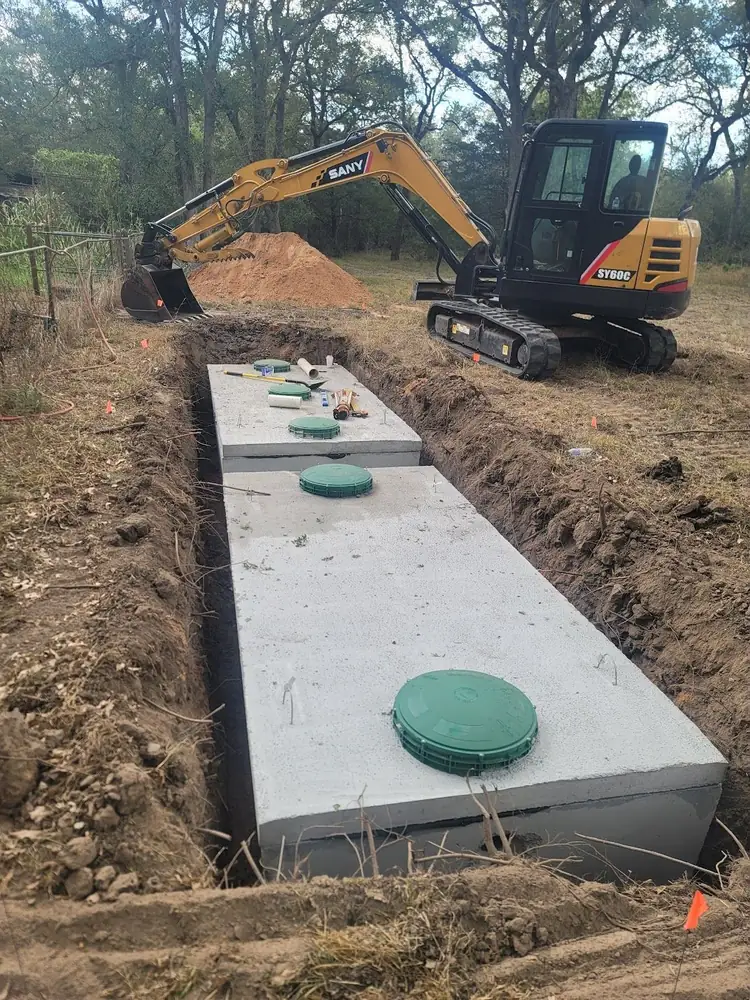 An excavator beside a long concrete septic tank set in a fresh trench