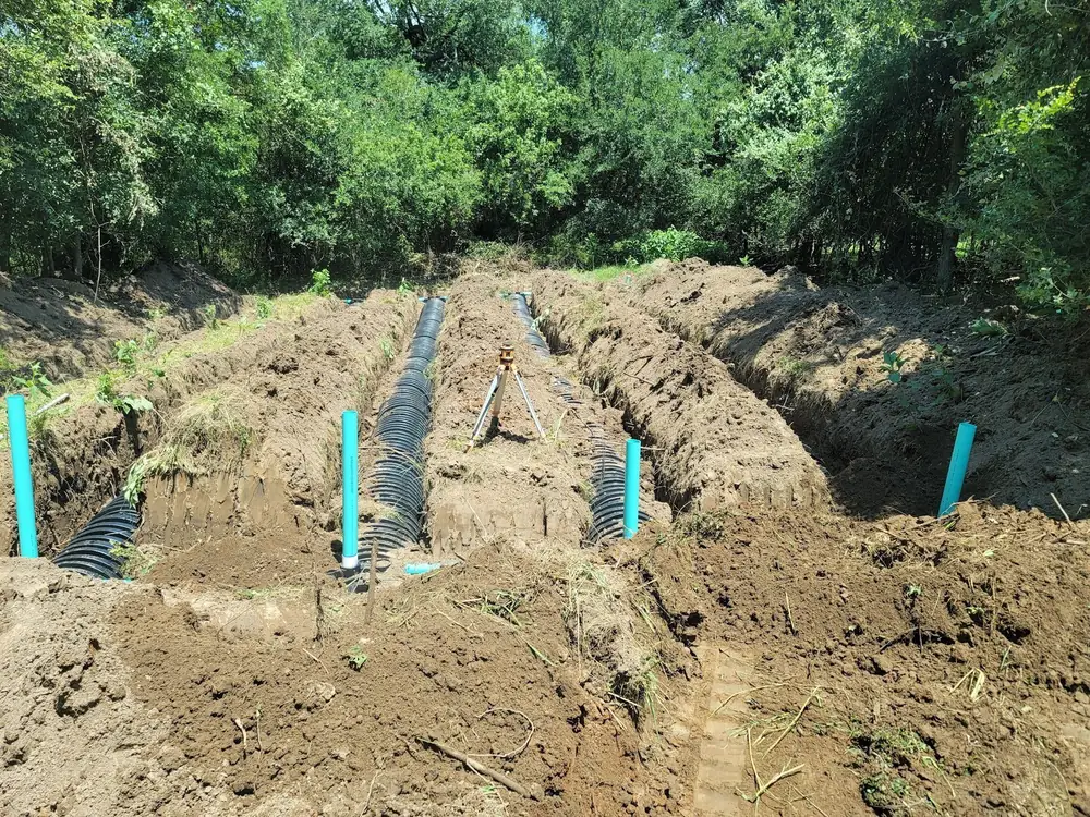Open drain-field trenches with black leaching chambers and blue inspection ports, trees behind